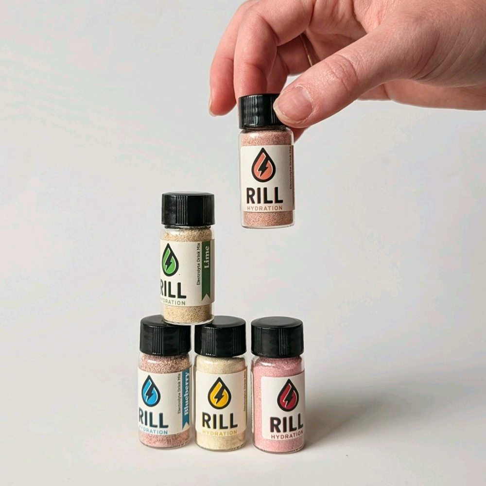 Hand grabbing a single serving of Rill Hydration Eelctrolyte Drink Mix in little jars

