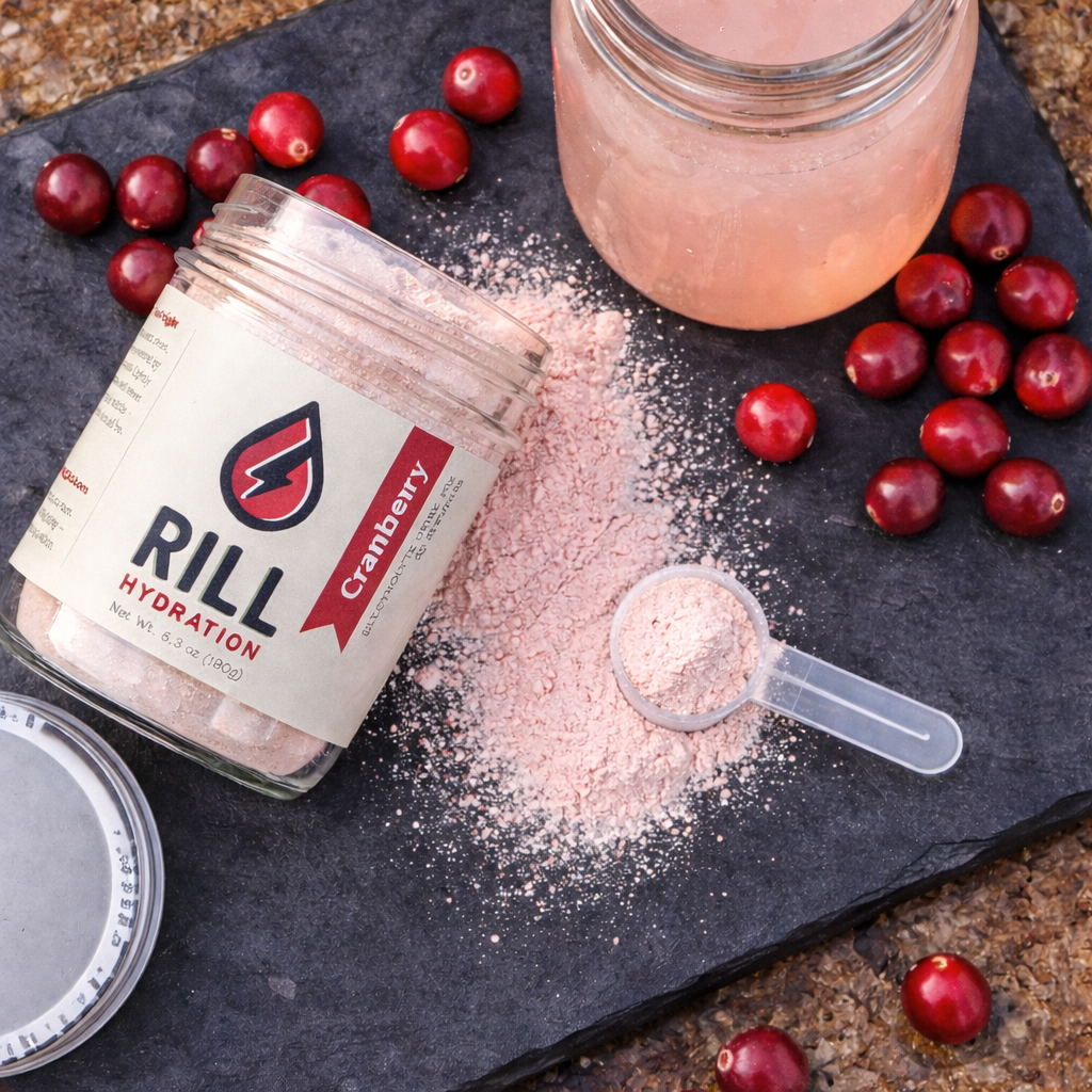 Rill Hydration cranberry powder with a scoop, jar, and cranberries on a dark surface