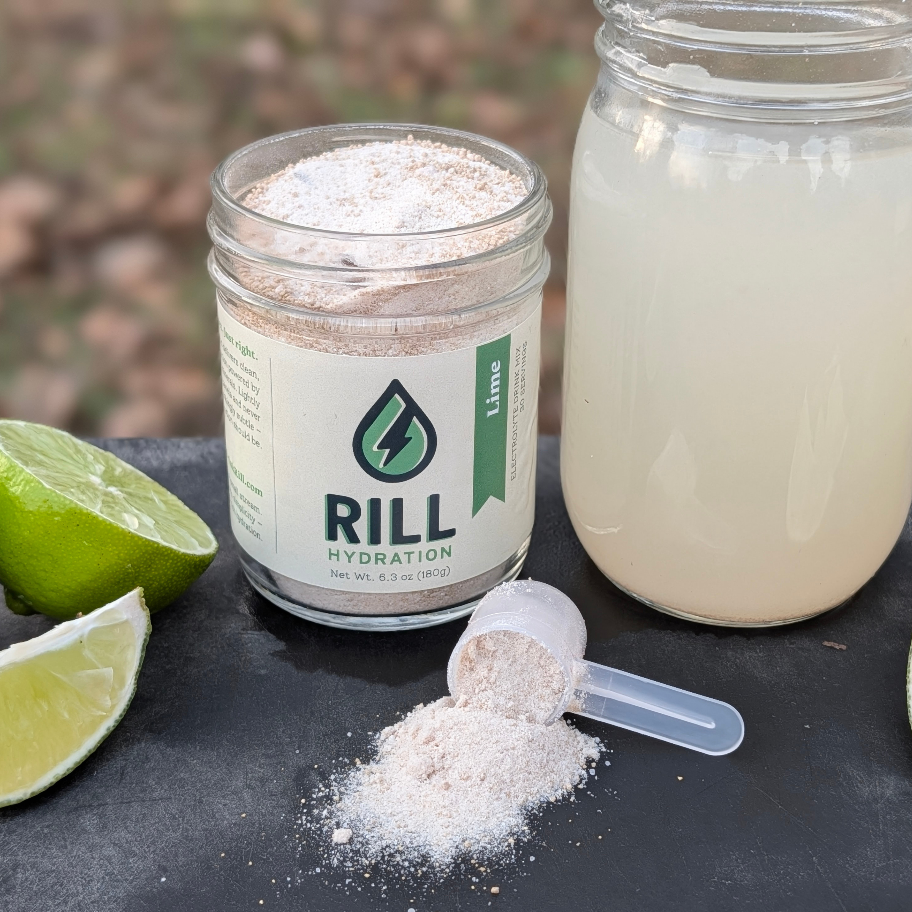 Jar of RILL Hydration powder with a lime and a scoop on a dark surface