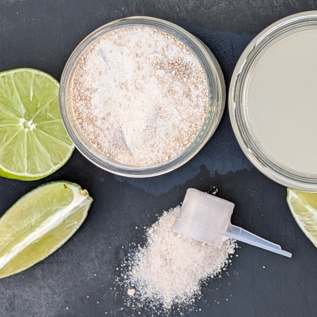 Overhead view of Lime Rill Hydration electrolyte drink mix, cut limes, a scoop of powder on a black board 
